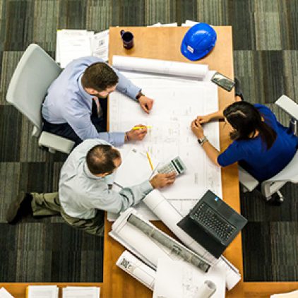Three workers discussing building plans at a conference table